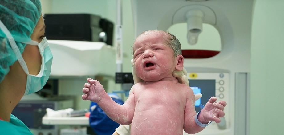 dziecko po porodzie w dłoniach personelu medycznego